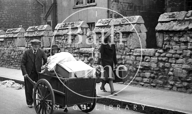 An elderly couple are helped moving their possessions along Upper Borough Walls, Bath 1942