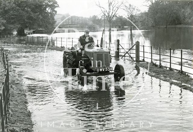 A farmer drives his tractor through the floods c.1960