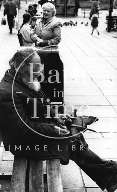 A man on a bench feeding pigeons c.1980