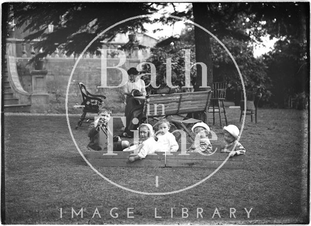 Children and their nanny in a garden paying c.1915