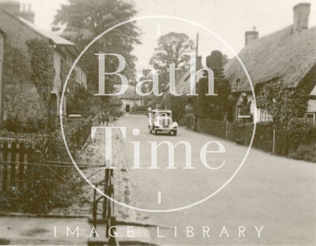 The photographer's car in an unidentified village with thatched cottages c.1930