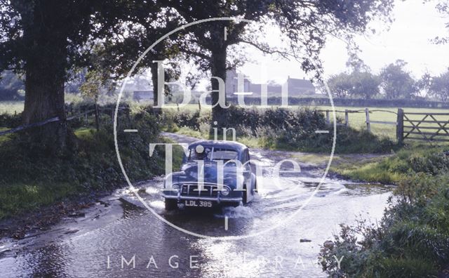 Negotiating a flooded part of the road in a Morris Minor c.1965