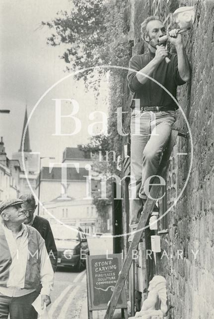 A stone mason carving a gargoyle head into a wall on Walcot Street, Bath 1993