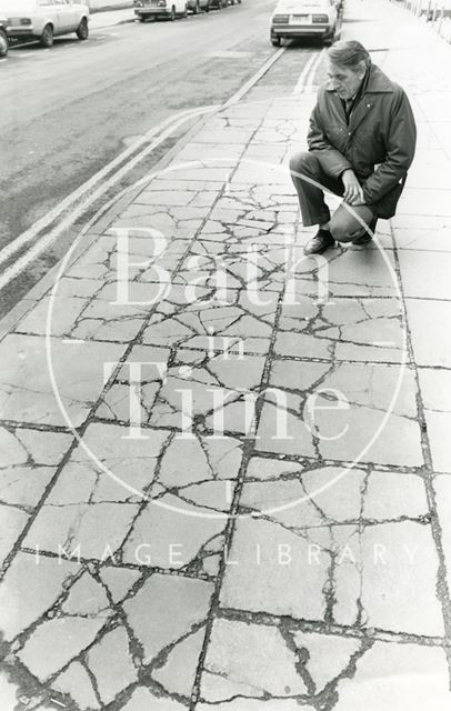 Man looking at pavement cracks left by lorries on Monmouth Street, Bath 1987