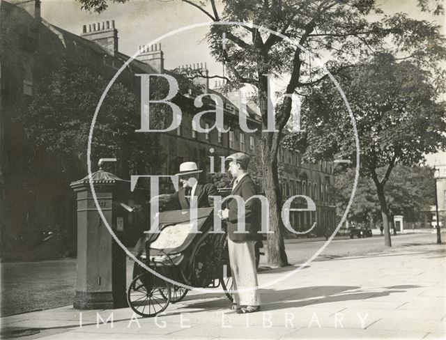 A man in a Bath chair posts a letter in the tree-line Great Pulteney Street, Bath c.1930