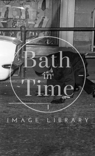 A policeman searching under a car for bombs, High Street, Bath 1974